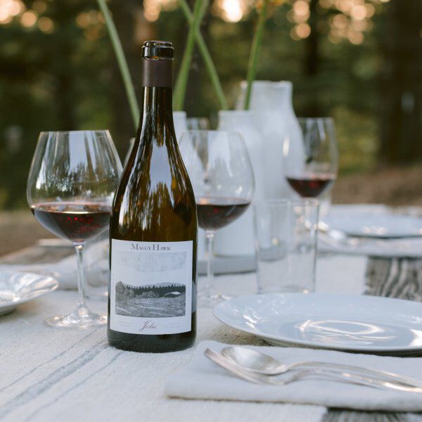 A bottle of Maggy Hawk on table surrounded by glasses of wine.